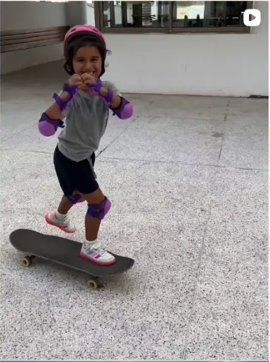 Young skater in a pink helmet and pads standing on a skateboard