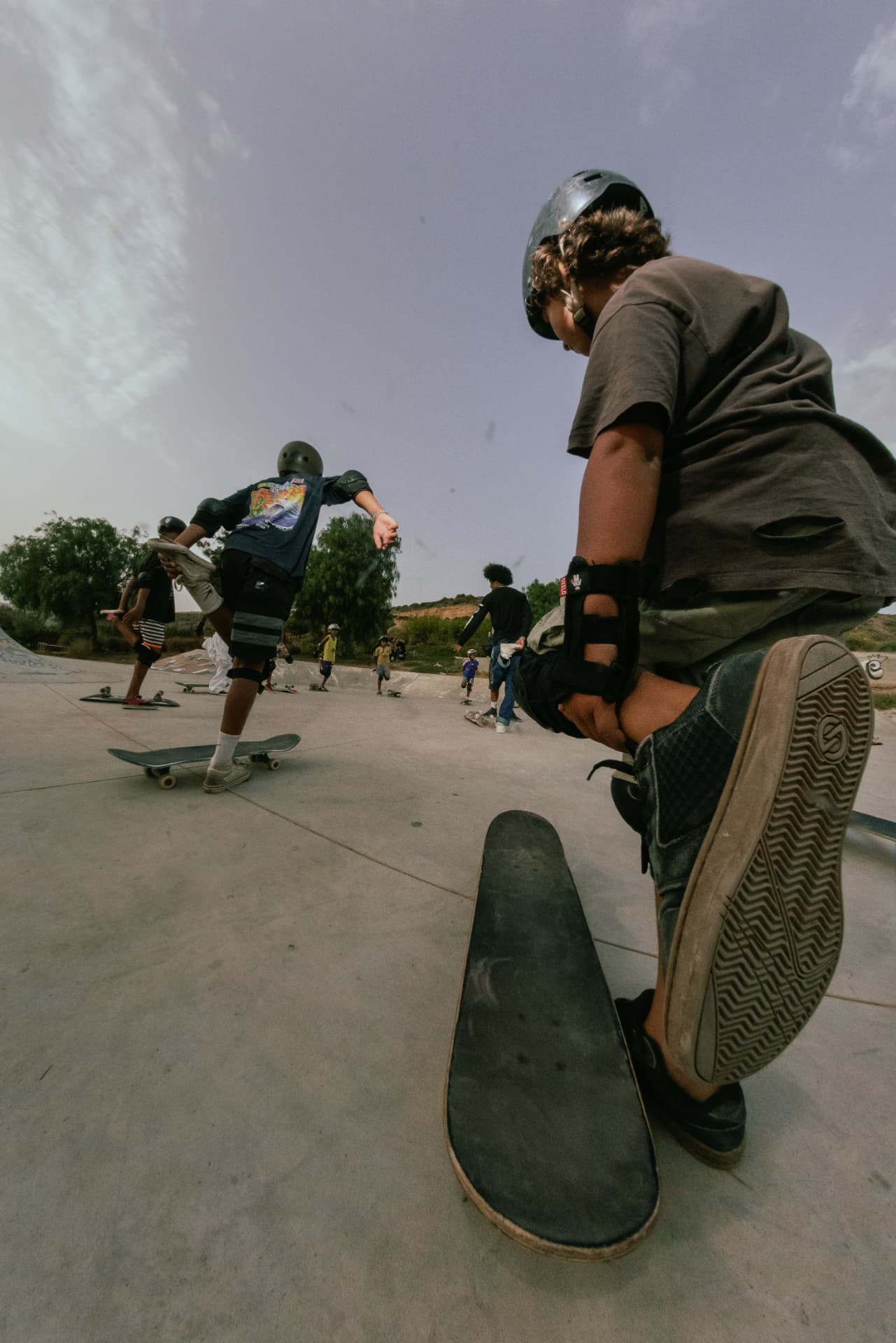 Kids in helmets and pads practising drop-ins on the skatepark flat during a coaching session