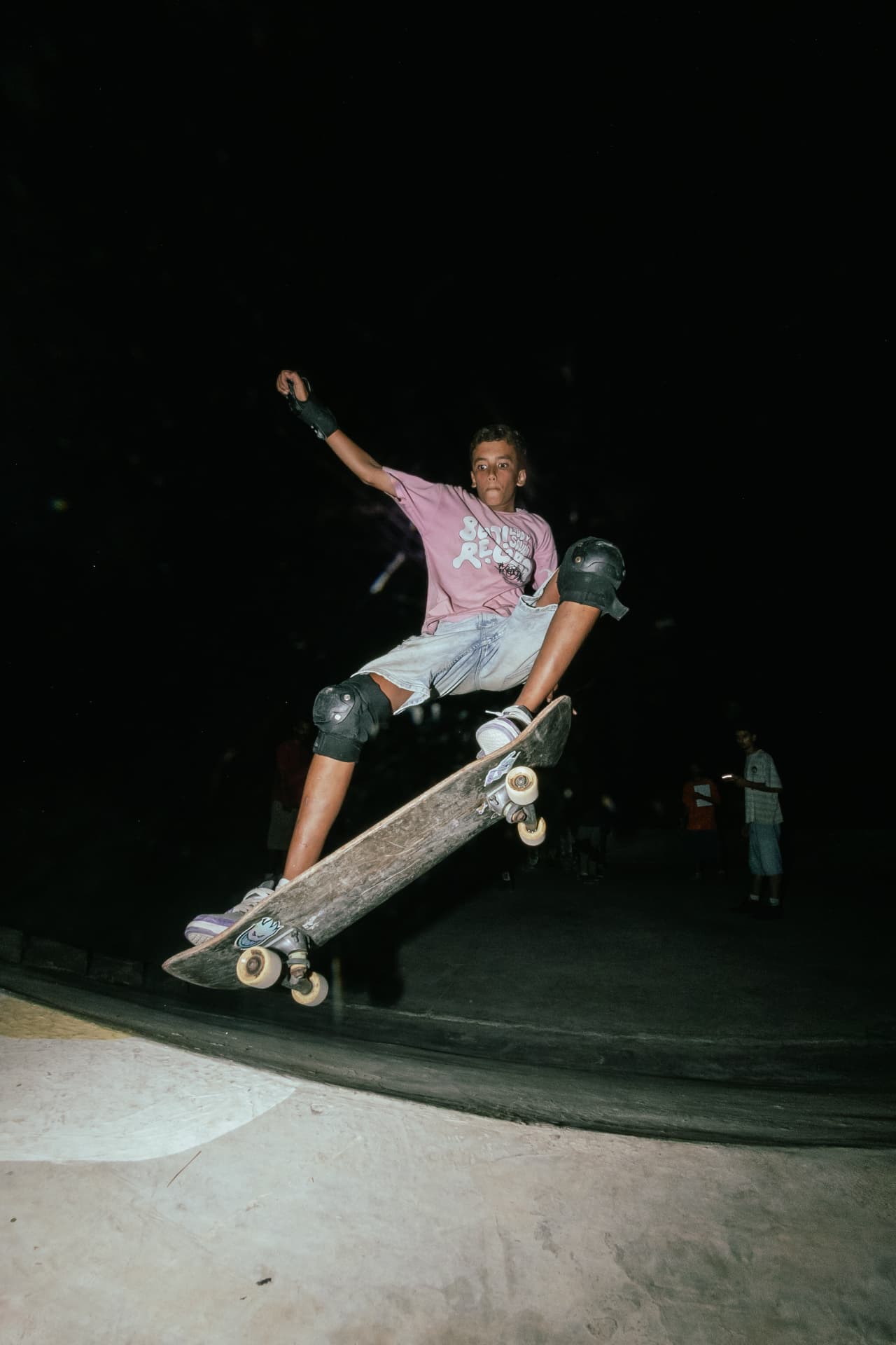 Teen skater catching air out of the bowl under the floodlights